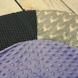 May include: A round, multi-colored play mat with three different fabric patterns. One section is black with white polka dots, another is gray with white deer silhouettes, and the third is a soft purple with a textured surface.