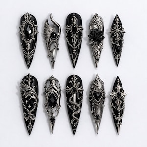 May include: A collection of ten black and silver gothic-style nail art designs. Each nail features intricate embellishments, including crosses, chains, and ornate filigree, with a variety of black gemstones and a rose.