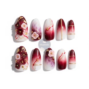 May include: A set of ten artificial nails with a variety of designs. Some nails feature a gradient of red and white, while others have floral embellishments, gold accents, and a marble effect. The nails are oval-shaped.