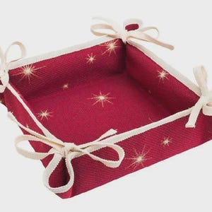 Könnte beinhalten: Ein quadratischer, roter Stoffkorb mit weißer Bordüre und Sternenmuster. Die Ecken sind mit weißen Schleifen gebunden. Der Korb ist zum Halten von Gegenständen bestimmt.