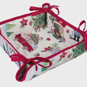 May include: A square fabric basket with a festive Christmas theme. The basket features a cream-colored background with red trim and ties at the corners. The fabric is patterned with red trucks, Christmas trees, and other holiday motifs.
