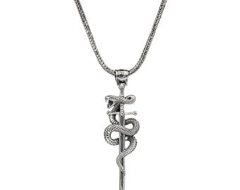May include: Silver-toned pendant necklace featuring a snake coiled around a sword. The snake has an open mouth, and the sword has a detailed hilt. The chain is a woven design. A gothic-inspired piece of jewelry.
