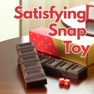Può includere: Un giocattolo a scatto marrone che ricorda una barretta di cioccolato, con un design segmentato. L'immagine mostra anche due dadi rossi e confezioni regalo con dettagli dorati e rossi. Il testo sull'immagine recita "Satisfying Snap Toy."