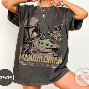 Pu&ograve; includere: T-shirt grigio scuro con grafica di The Mandalorian e Grogu di Star Wars. Il design include la scritta "MANDALORIAN THIS IS THE WAY" in stile vintage. La maglietta ha maniche corte e una vestibilit&agrave; ampia.