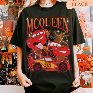 Może przedstawiać: Czarny t-shirt z kr&oacute;tkim rękawem z nadrukiem graficznym przedstawiającym trzy czerwone samochody wyścigowe z numerem 95 i napisem MCQUEEN w kolorze pomarańczowym. Wz&oacute;r zawiera błyskawice i gwiazdki na ciemnym, dymnym tle.