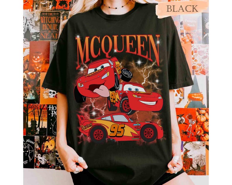 Może przedstawiać: Czarny t-shirt z kr&oacute;tkim rękawem z nadrukiem graficznym przedstawiającym trzy czerwone samochody wyścigowe z numerem 95 i napisem MCQUEEN w kolorze pomarańczowym. Wz&oacute;r zawiera błyskawice i gwiazdki na ciemnym, dymnym tle.