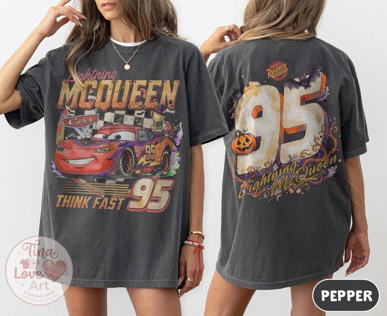 May include: A charcoal gray t-shirt featuring a graphic of Lightning McQueen from Cars on the front with the text Lightning McQueen and Think Fast 95. The back displays a large number 95 with a pumpkin, a bat, and the text Lightning McQueen.
