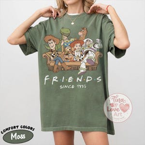 Peut inclure: Un t-shirt vert mousse avec une impression graphique repr&eacute;sentant divers personnages anim&eacute;s assis sur un canap&eacute;. Le texte "FRIENDS SINCE 1995" est imprim&eacute; sous l'illustration. Le t-shirt a un col rond et des manches courtes, coupe d&eacute;contract&eacute;e.