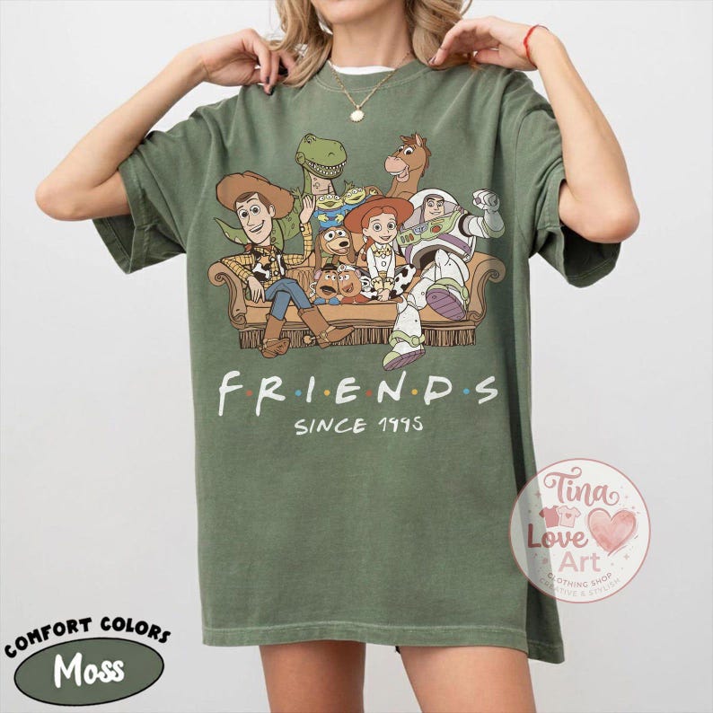 Peut inclure: Un t-shirt vert mousse avec une impression graphique repr&eacute;sentant divers personnages anim&eacute;s assis sur un canap&eacute;. Le texte "FRIENDS SINCE 1995" est imprim&eacute; sous l'illustration. Le t-shirt a un col rond et des manches courtes, coupe d&eacute;contract&eacute;e.