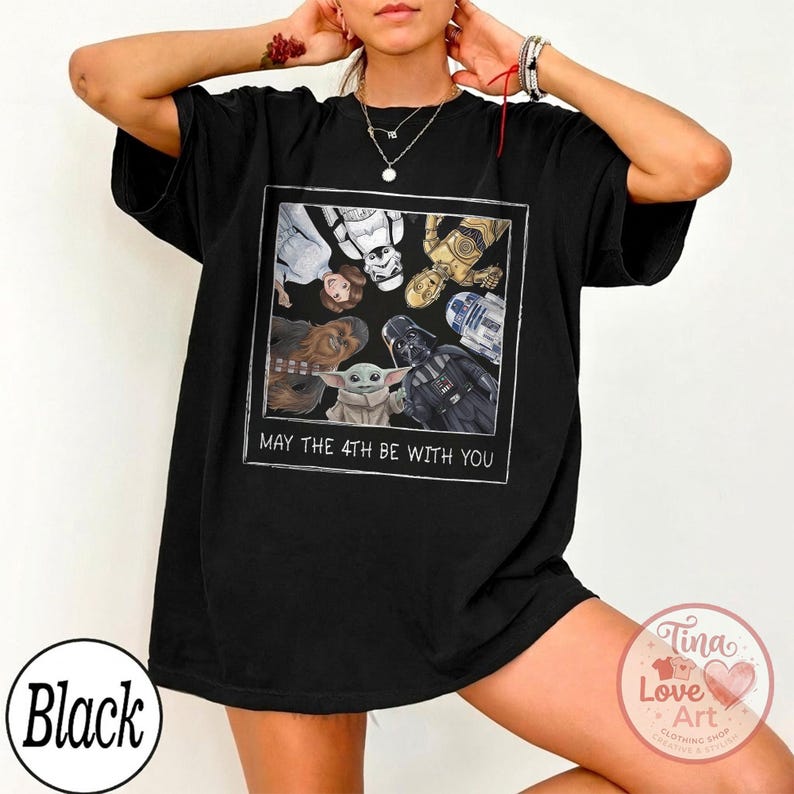 May include: Black t-shirt featuring a framed graphic of Star Wars characters including Darth Vader, Yoda, and R2-D2. The text "MAY THE 4TH BE WITH YOU" is printed below the graphic. The shirt has a relaxed fit.