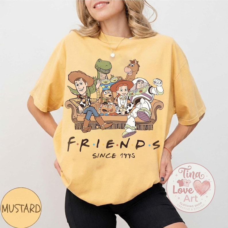 Peut inclure: Un t-shirt jaune moutarde &agrave; manches courtes avec une impression graphique de divers personnages de jouets anim&eacute;s assis sur un canap&eacute;. Sous les personnages, le texte indique FRIENDS SINCE 1995. Le t-shirt a un col rond et une coupe d&eacute;contract&eacute;e.