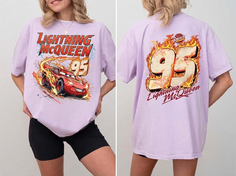 May include: A light purple t-shirt featuring a graphic of the red race car Lightning McQueen with the number 95 on the front. The back of the shirt displays the number 95 surrounded by flames and the text Lightning McQueen and Rust-eze.