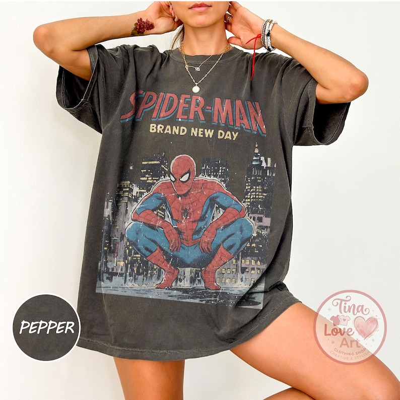 May include: Dark gray t-shirt featuring a graphic of Spider-Man in a crouching pose, with the words "SPIDER-MAN BRAND NEW DAY" above. The design includes a cityscape background. The shirt is oversized.