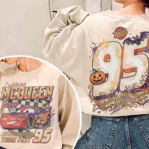 May include: A beige crewneck sweatshirt featuring a graphic of Lightning McQueen on the front with the text Lightning McQueen and Think Fast 95. The back displays a large number 95, a pumpkin, a bat, and the text Lightning McQueen.