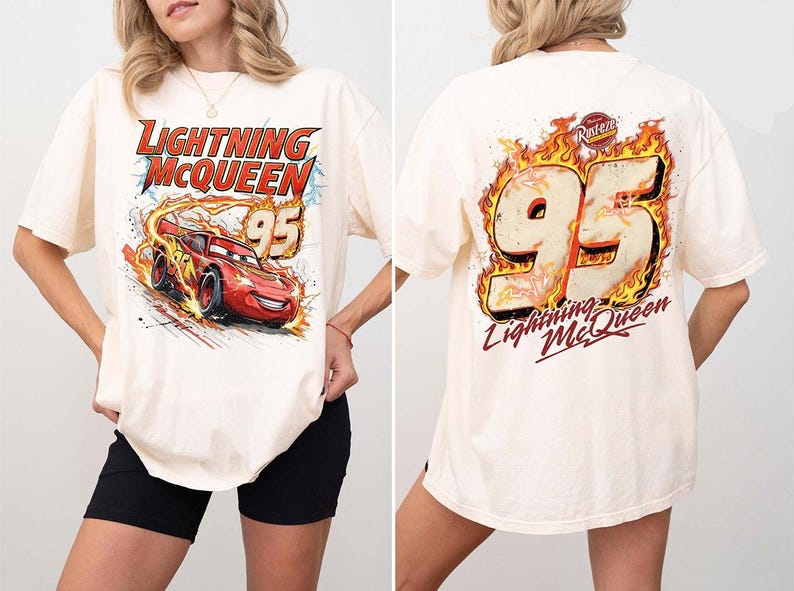 May include: An off-white short-sleeve t-shirt featuring a graphic of the red race car Lightning McQueen with the number 95 on the front. The back of the shirt displays a large number 95 surrounded by flames and the text Lightning McQueen.