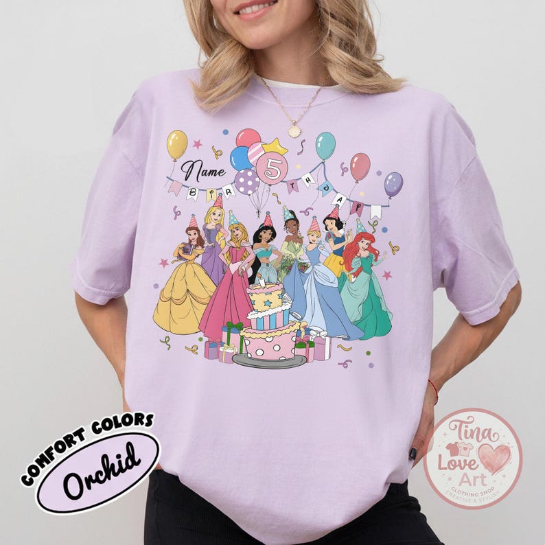 May include: Orchid Comfort Colors t-shirt featuring a colorful graphic of Disney princesses around a birthday cake. The design includes balloons, a banner that says "Name", and the number "5". The shirt has a relaxed fit.