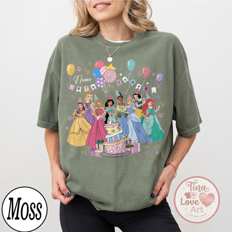 May include: Olive green t-shirt featuring a colorful graphic of Disney princesses, balloons, and a birthday cake. The number 5 is prominently displayed, with the word "Name" above. The shirt is from Tina Love Art.
