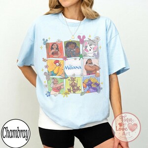 Puede incluir: Camiseta azul claro con una cuadr&iacute;cula de personajes de Moana. El dise&ntilde;o incluye im&aacute;genes de Moana, Maui, Pua, Hei Hei y otros, con la palabra "Moana" en el centro. La camiseta tiene cuello redondo y mangas cortas.