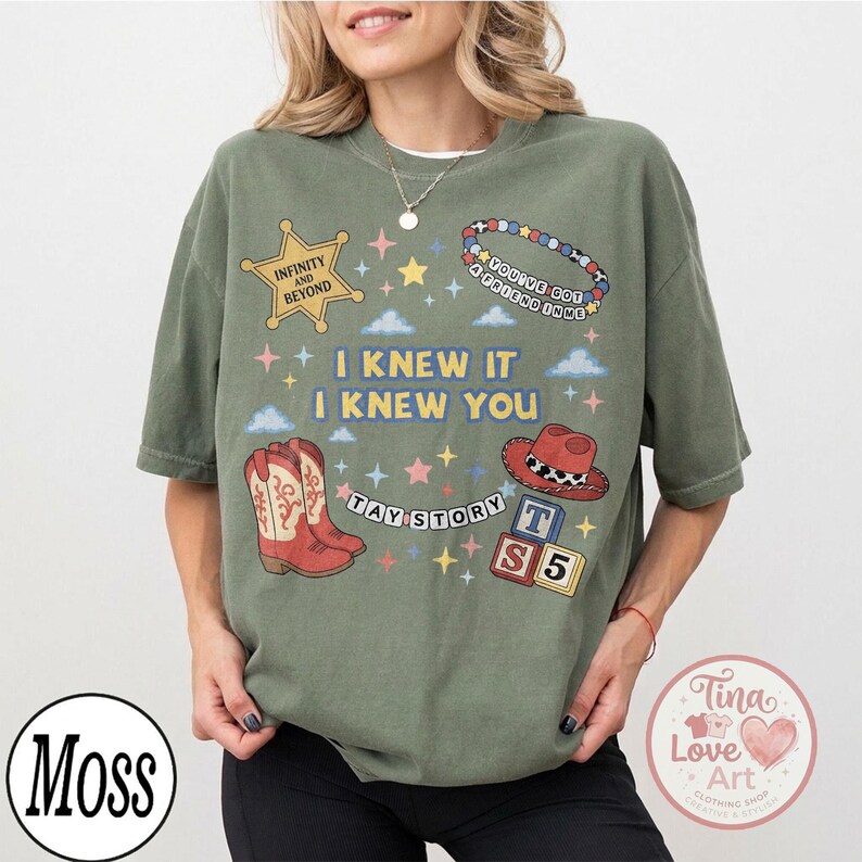 May include: An olive green t-shirt featuring a graphic print with a yellow sheriff star labeled "INFINITY AND BEYOND," a beaded bracelet with "YOU'VE GOT A FRIEND IN ME," red cowboy boots, a red hat, blocks with "T S 5," and "I KNEW IT I KNEW YOU TAY STORY."