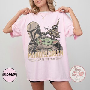 Pu&ograve; includere: T-shirt rosa chiaro con grafica di The Mandalorian e Grogu, con la scritta "MANDALORIAN THIS IS THE WAY". Il design include un'astronave e un casco. La maglietta ha una vestibilit&agrave; comoda e oversize.