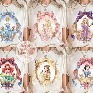 May include: Cream-colored t-shirts featuring watercolor portraits of Disney princesses within ornate frames. Each princess is surrounded by a decorative bow and ribbon. The shirts have a round neckline and short sleeves.