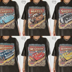 May include: A collection of six black t-shirts, each featuring a different vintage-style graphic of a character from the movie Cars, including Sally Carrera, Tow Mater, Sheriff, Doc Hudson, Lightning McQueen, and Cruz Ramirez with race text.