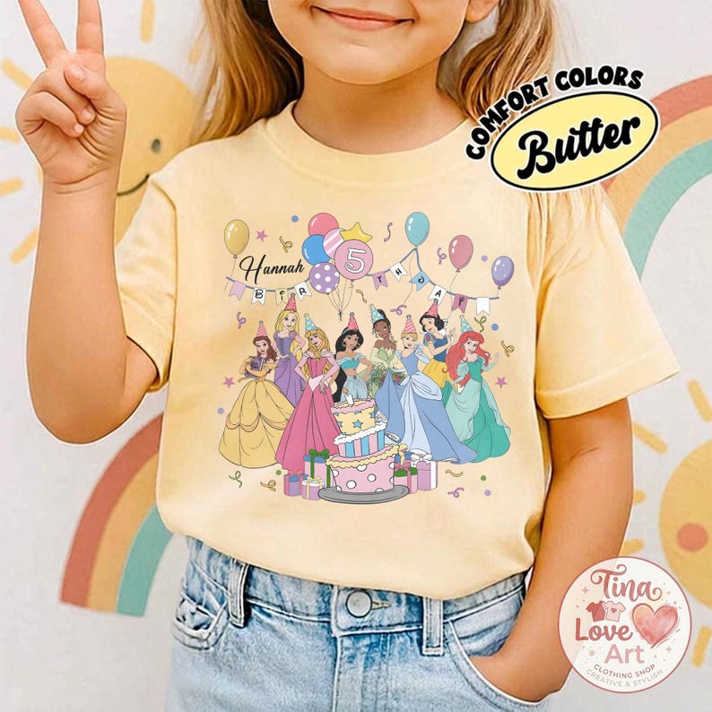 May include: Yellow t-shirt featuring a group of cartoon princesses around a birthday cake. The shirt has the text "Hannah Birthday 5" and the words "Comfort Colors Butter" in a circle.