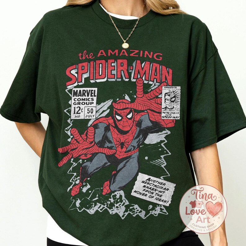 Może przedstawiać: Ciemnozielona koszulka z grafiką komiksową Spider-Mana w stylu vintage. Projekt zawiera tekst "the AMAZING SPIDER-MAN" i "MARVEL COMICS GROUP". Grafika jest w kolorze czerwonym, czarnym i szarym.