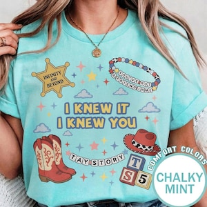 May include: A mint green t-shirt featuring a graphic print with a yellow sheriff star labeled Infinity and Beyond, a beaded bracelet reading You've Got a Friend in Me, cowboy boots, a red hat, alphabet blocks, and the text I Knew It I Knew You.