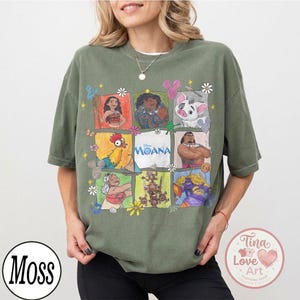 Puede incluir: Camiseta verde oliva con un dise&ntilde;o de cuadr&iacute;cula colorida con personajes de la pel&iacute;cula de Disney "Moana". El dise&ntilde;o incluye ilustraciones de Moana, Maui, Pua, Hei Hei y otros personajes. La palabra "Moana" est&aacute; impresa en blanco. La camiseta tiene mangas cortas.