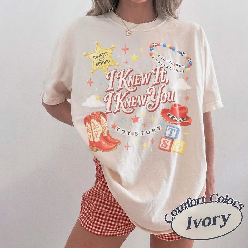Puede incluir: Una camiseta de manga corta color marfil con un estampado gr&aacute;fico que incluye el texto "I KNEW IT, I KNEW YOU", "TOY STORY", "INFINITY AND BEYOND" y "YOU'VE GOT A FRIEND IN ME". El dise&ntilde;o presenta una estrella amarilla, botas rojas y bloques.