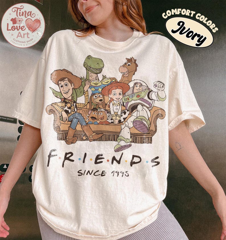 Peut inclure: Un t-shirt ivoire avec une impression graphique repr&eacute;sentant divers personnages anim&eacute;s assis sur un canap&eacute;. Sous les personnages, le texte indique "FRIENDS" avec des points color&eacute;s entre les lettres, suivi du texte "SINCE 1995" en noir.