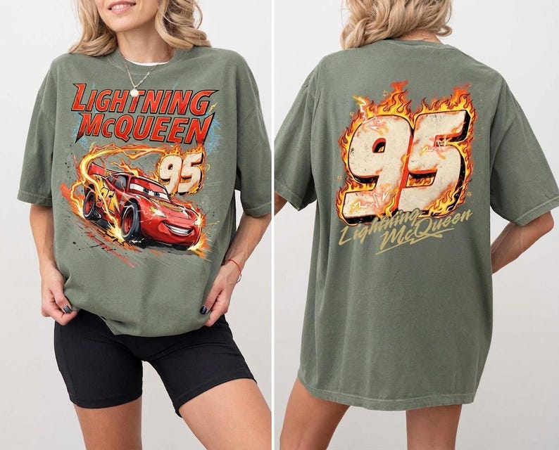May include: An olive green t-shirt featuring a graphic of the red race car Lightning McQueen with the text Lightning McQueen and the number 95 on the front. The back displays a large number 95 surrounded by flames with the text Lightning McQueen.