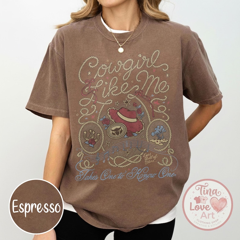 Pu&ograve; includere: Una t-shirt a maniche corte color marrone espresso con una stampa grafica che riporta il testo Cowgirl Like Me, Eyes full of Stars e Takes One to Know One. Il design include un cappello rosso, un ferro di cavallo e motivi a corda.
