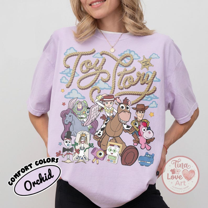 Op de afbeelding: Een lichtpaars t-shirt met een grafische print van Toy Story-personages, waaronder Woody, Jessie, Buzz Lightyear, Bullseye en Forky. De tekst Toy Story staat in een touwachtig lettertype boven de personages met blauwe wolken.