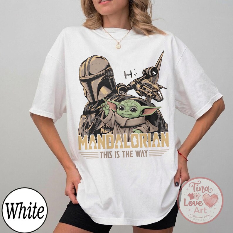 Pu&ograve; includere: T-shirt bianco con grafica di The Mandalorian e Grogu, con la scritta "MANDALORIAN THIS IS THE WAY". Il design include un'astronave e un casco. La maglietta ha una vestibilit&agrave; ampia.
