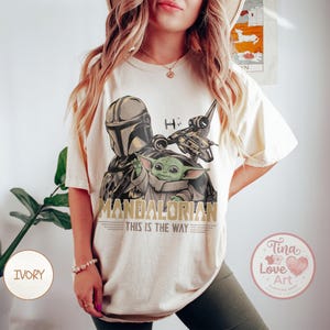 Pu&ograve; includere: T-shirt color avorio con grafica di The Mandalorian, Grogu e un'astronave. I testi "MANDALORIAN" e "THIS IS THE WAY" sono stampati sotto l'immagine. La maglietta ha una vestibilit&agrave; ampia.