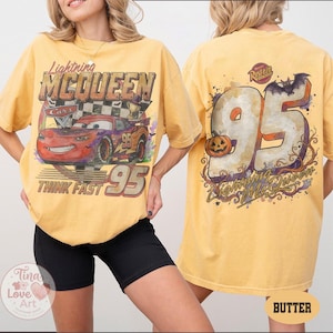 May include: A butter yellow t-shirt featuring a graphic of Lightning McQueen from Cars on the front with the text Lightning McQueen, Think Fast, and 95. The back displays a large 95 with a pumpkin, a bat, and the text Rusteze and Lightning McQueen.