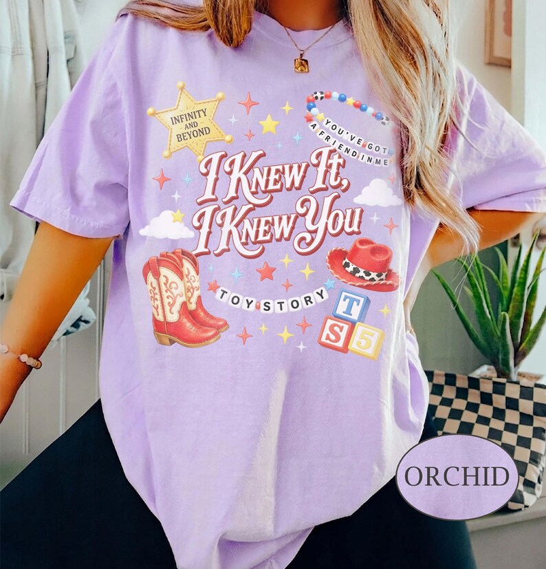 Puede incluir: Una camiseta de color morado claro con un estampado gr&aacute;fico que incluye el texto I KNEW IT, I KNEW YOU, TOY STORY, INFINITY AND BEYOND y YOU'VE GOT A FRIEND IN ME. El dise&ntilde;o muestra una estrella de sheriff, botas, sombrero y bloques.