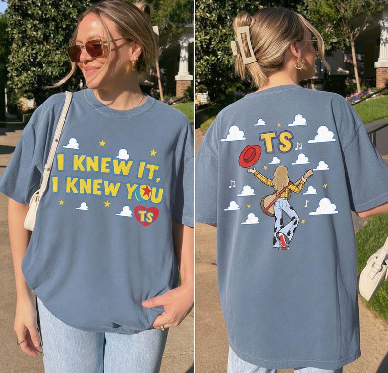 K&ouml;nnte beinhalten: Ein blaues T-Shirt mit Grafikdruck. Die Vorderseite zeigt den Text I KNEW IT, I KNEW YOU mit einem Ball-Symbol und einem roten Herz mit den Buchstaben TS. Die R&uuml;ckseite zeigt eine Person mit Gitarre, rotem Hut und den Buchstaben TS zwischen Wolken.