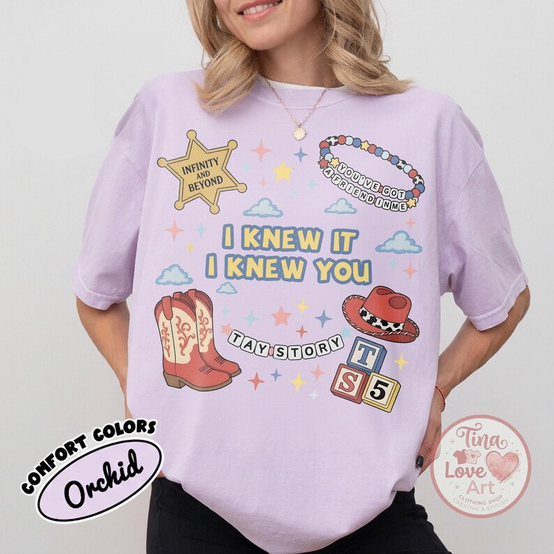 May include: A light purple t-shirt featuring a graphic print with a yellow sheriff star labeled Infinity and Beyond, a beaded bracelet, cowboy boots, a red hat, and blocks with the text TAY STORY and I KNEW IT I KNEW YOU with colorful stars.