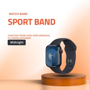 May include: A midnight blue sport watch band made from high-performance fluoroelastomer. The watch face displays a dark blue screen with white hands. The watch is displayed on a small, round wooden stand.