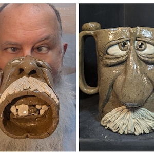 May include: A handcrafted ceramic mug with a sculpted face design. The mug features a detailed face with a prominent nose, wide eyes, and a white mustache. The mug is brown with a textured surface and a large handle.