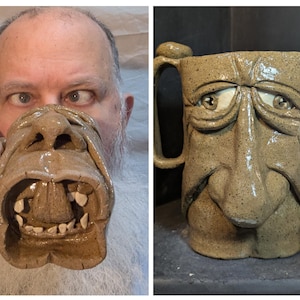 May include: A tan ceramic mug with a sculpted face design. The mug features a handle and is approximately 5 inches tall. The face has detailed eyes, a nose, and an open mouth with teeth. The mug is held up to a person's face.