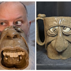 May include: A unique, handmade ceramic mug with a sculpted face design. The mug features a detailed face with expressive eyes, a large nose, and an open mouth revealing teeth. The mug is approximately 5 inches tall and has a handle.