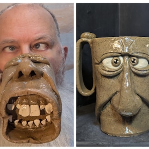 May include: A tan ceramic mug with a sculpted face design. The mug features a handle and measures approximately 5 inches tall. The face has large eyes, a nose, and an open mouth with teeth. The mug is handmade and has a rustic appearance.
