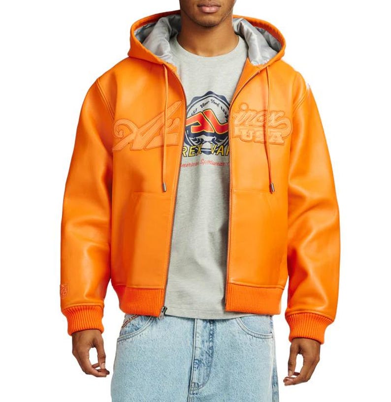 May include: Bright orange leather hooded jacket with a zip-up front, ribbed cuffs, and a matching ribbed hem. The jacket features embossed lettering and a logo patch on the chest. The hood has a silver lining.