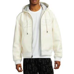 May include: Cream-colored zip-up hoodie with a gray interior lining. The jacket features embroidered text on the chest and a ribbed hem and cuffs. The model is wearing a white t-shirt underneath.