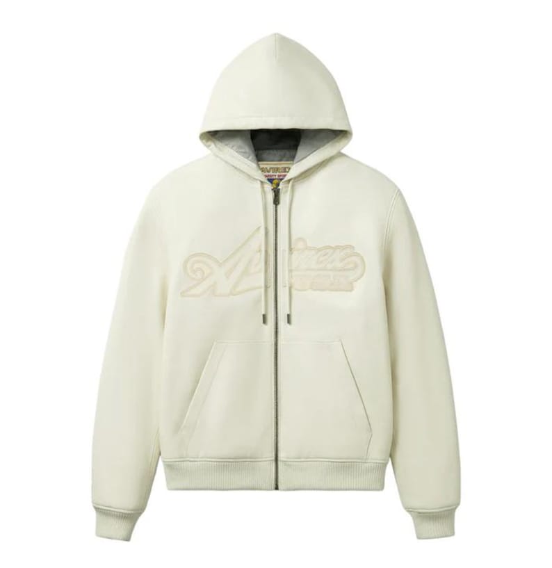 May include: Cream-colored zip-up hoodie with a hood and front pockets. The hoodie features the word "Aviation" in a stylized, raised design across the chest. The zipper is silver, and the interior of the hood is a darker gray.