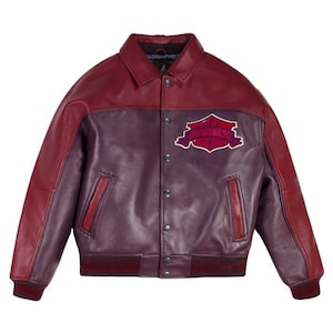 K&ouml;nnte beinhalten: Burgunderrote und violette Lederjacke mit Kragen und Knopfleiste. Die Jacke hat einen Aufn&auml;her auf der Brust mit dem Wort "AVIREX" in einer stilisierten Schriftart. Gerippte B&uuml;ndchen und Saum.